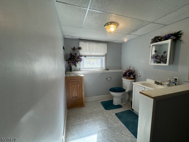 bathroom with toilet, baseboards, a drop ceiling, and vanity