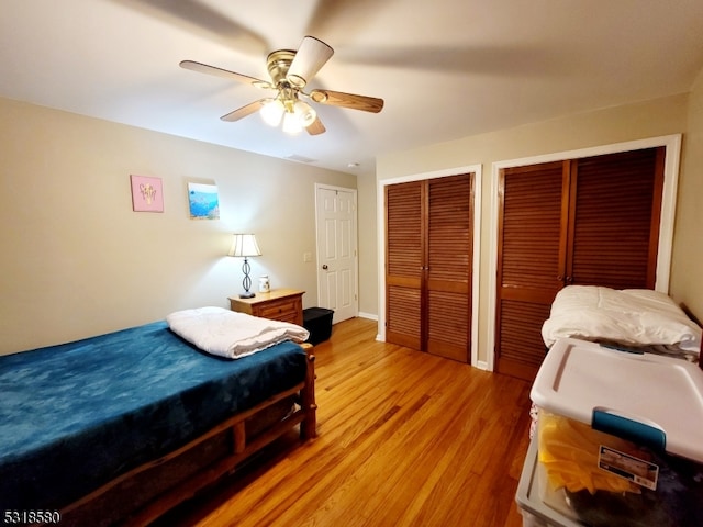 bedroom with multiple closets, light hardwood / wood-style floors, and ceiling fan