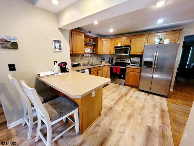 kitchen with backsplash, appliances with stainless steel finishes, light wood-type flooring, a kitchen bar, and kitchen peninsula