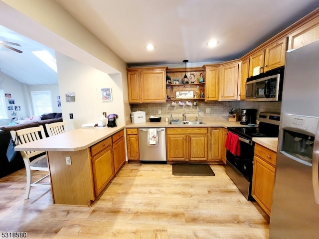 kitchen featuring backsplash, appliances with stainless steel finishes, a kitchen bar, light hardwood / wood-style floors, and kitchen peninsula