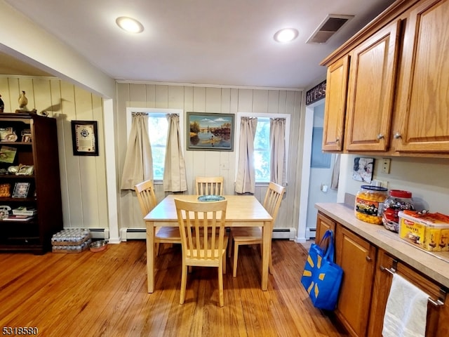 dining room with wood walls, light hardwood / wood-style floors, and a baseboard radiator