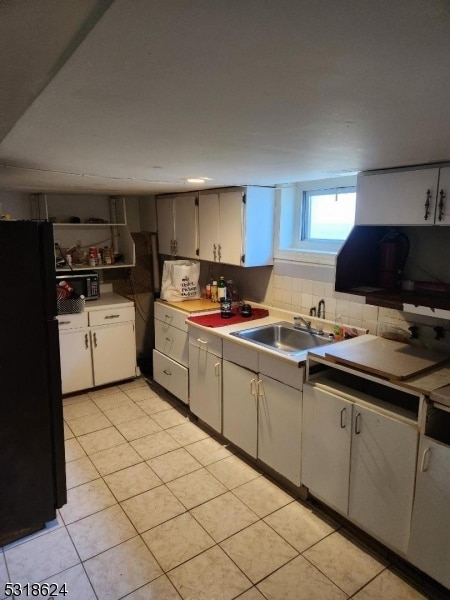 kitchen with light tile patterned floors, sink, black refrigerator, and tasteful backsplash