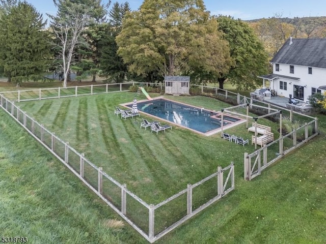 view of swimming pool featuring a storage unit, a fenced backyard, an outbuilding, and a yard