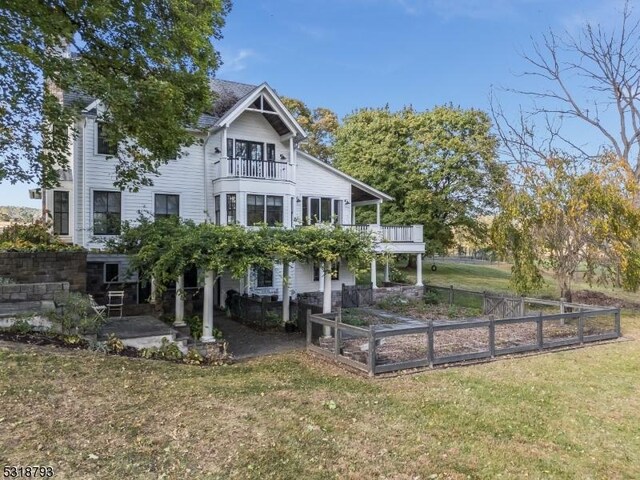rear view of property featuring fence, a patio area, a lawn, a vegetable garden, and a balcony