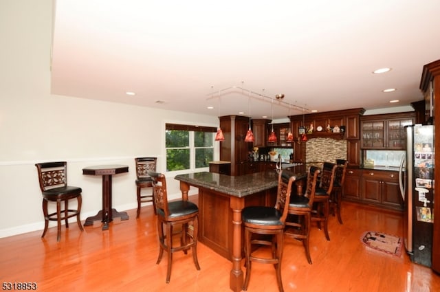 kitchen with a breakfast bar area, stainless steel refrigerator, decorative light fixtures, and light hardwood / wood-style floors