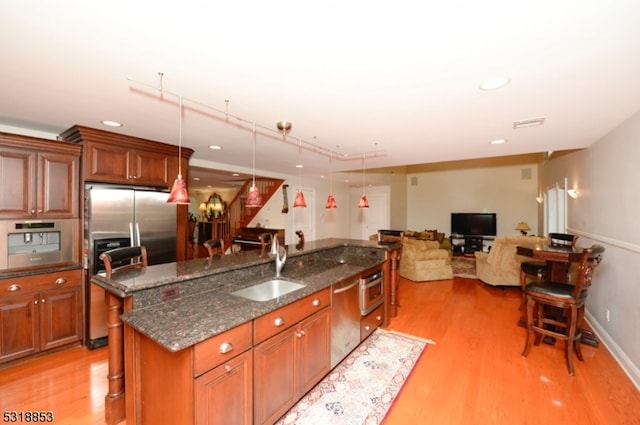 kitchen featuring decorative light fixtures, appliances with stainless steel finishes, a kitchen island with sink, and light hardwood / wood-style floors