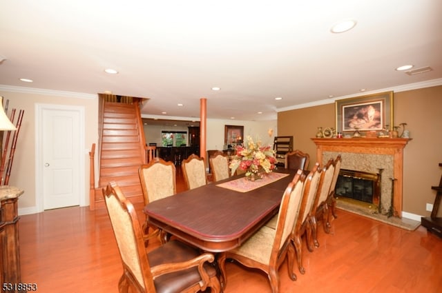 dining area featuring wood-type flooring, crown molding, and a high end fireplace