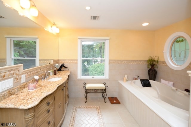 bathroom with tile patterned flooring, a relaxing tiled tub, vanity, and a wealth of natural light