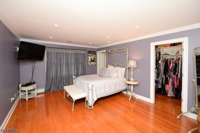 bedroom with hardwood / wood-style flooring, a spacious closet, crown molding, and a closet