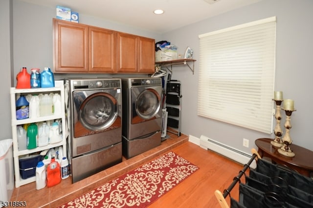 laundry room featuring light wood-type flooring, baseboard heating, washing machine and clothes dryer, and cabinets