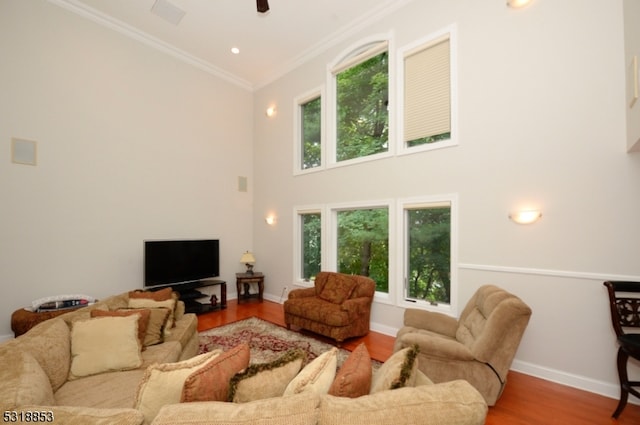 living room with ornamental molding, hardwood / wood-style flooring, ceiling fan, and a towering ceiling