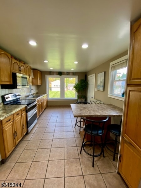 kitchen featuring appliances with stainless steel finishes, light stone counters, a wealth of natural light, and light tile patterned floors