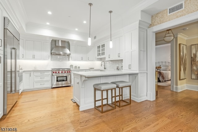 kitchen with wall chimney range hood, white cabinets, light wood-type flooring, and high end appliances