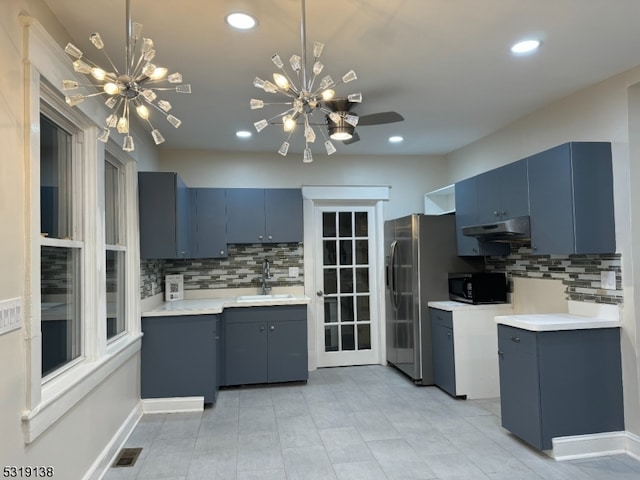 kitchen with stainless steel appliances, blue cabinetry, sink, decorative backsplash, and a chandelier