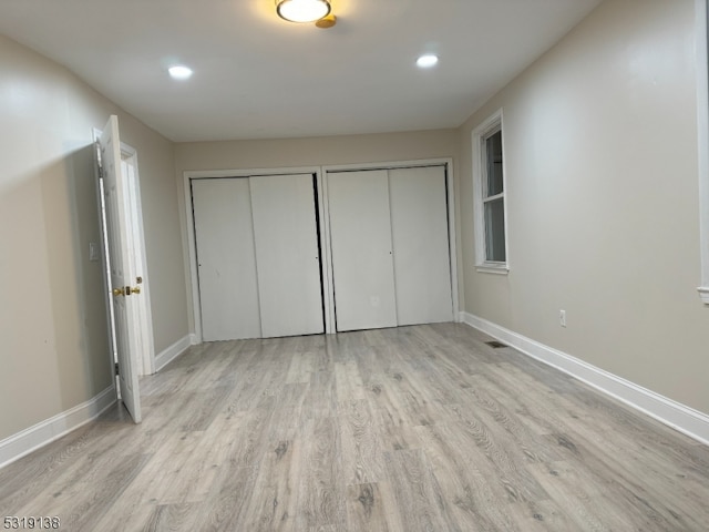 unfurnished bedroom with light hardwood / wood-style floors and multiple closets