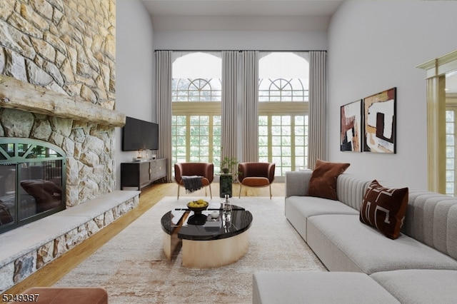 living room featuring light hardwood / wood-style flooring, a stone fireplace, and a towering ceiling