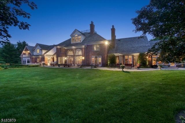 back house at dusk featuring a patio area and a lawn