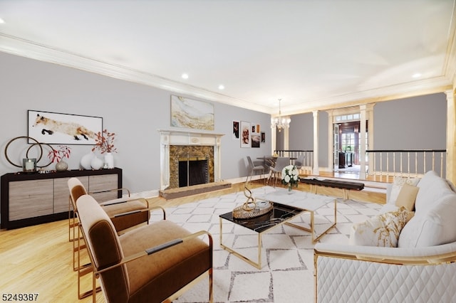 living room featuring a premium fireplace, an inviting chandelier, light hardwood / wood-style flooring, ornate columns, and crown molding