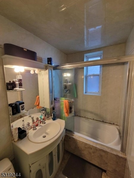 full bathroom featuring tile walls, toilet, combined bath / shower with glass door, and sink