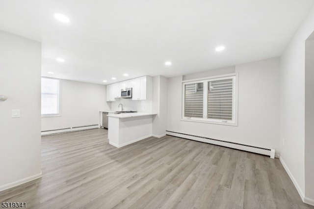 unfurnished living room featuring light hardwood / wood-style floors, baseboard heating, and sink