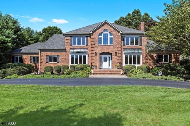 view of front of property with brick siding, a chimney, aphalt driveway, and a front yard