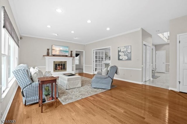 living area with light wood-style flooring, baseboards, crown molding, and a glass covered fireplace