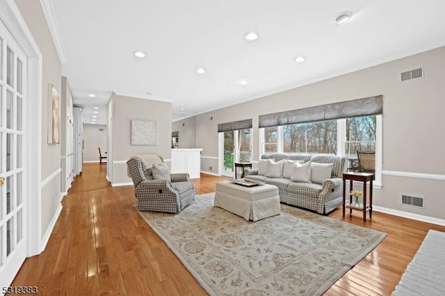 living area featuring baseboards, light wood-style flooring, visible vents, and crown molding