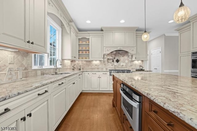 kitchen with light stone countertops, stainless steel oven, pendant lighting, and a sink