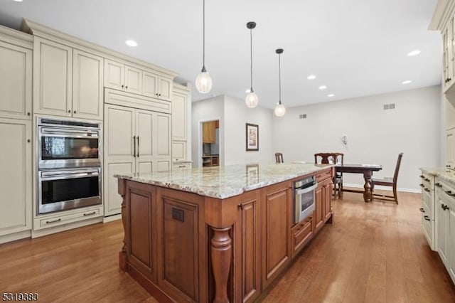 kitchen with paneled fridge, cream cabinets, stainless steel double oven, wood finished floors, and a center island