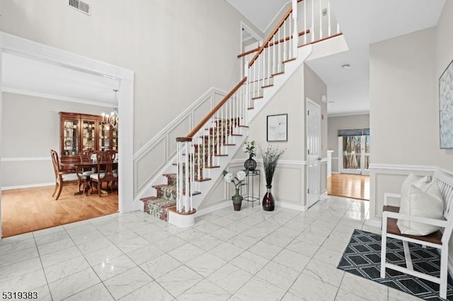 entryway with a decorative wall, visible vents, stairs, marble finish floor, and wainscoting