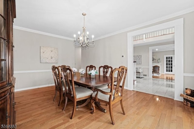 dining space featuring light wood-style floors, a notable chandelier, baseboards, and crown molding