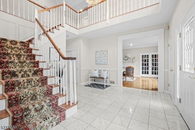 foyer entrance with stairway, a wainscoted wall, a decorative wall, and a towering ceiling