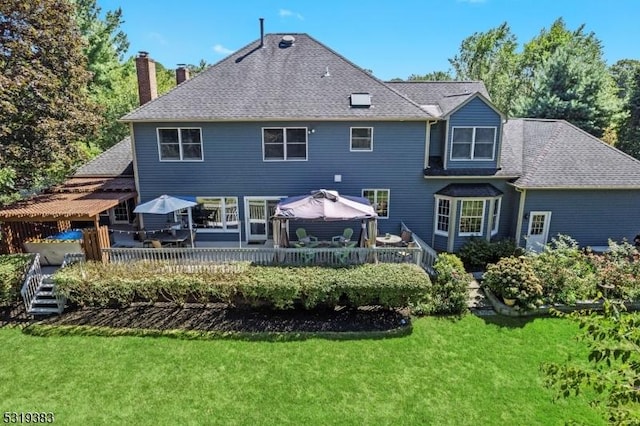 back of house with a shingled roof, a lawn, and a wooden deck