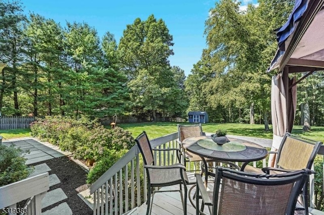 wooden deck featuring an outbuilding, outdoor dining area, fence, a yard, and a shed