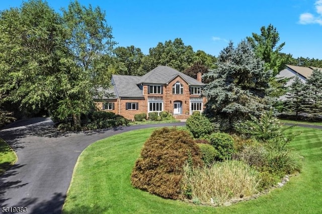 colonial home with a chimney, a front lawn, and aphalt driveway