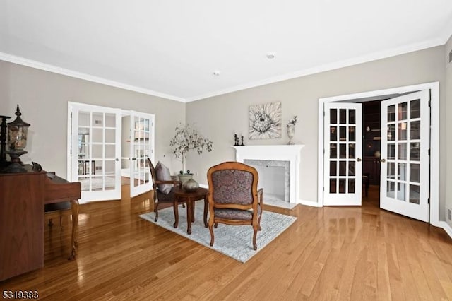 sitting room featuring a fireplace, ornamental molding, wood finished floors, and french doors