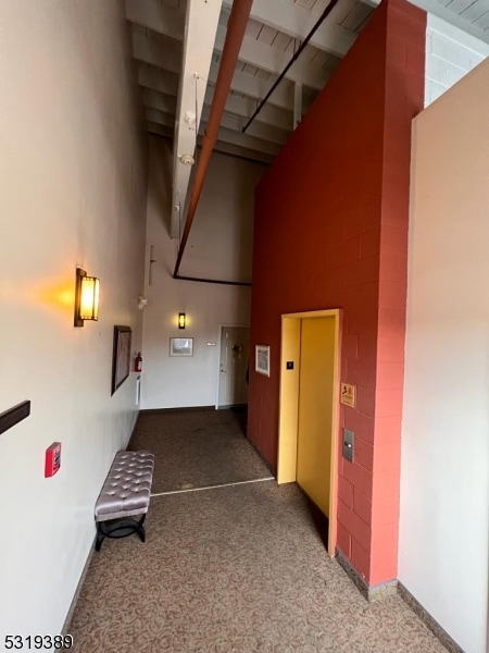 hallway with elevator, carpet flooring, and a high ceiling