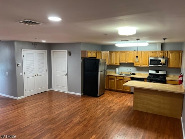 kitchen featuring kitchen peninsula, appliances with stainless steel finishes, dark wood-type flooring, pendant lighting, and sink