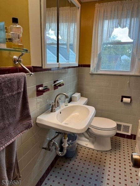 bathroom featuring toilet, sink, tile patterned floors, and tile walls