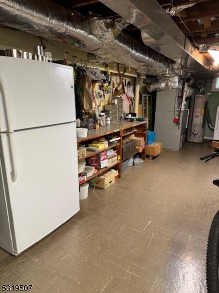 basement featuring water heater, heating unit, and white refrigerator