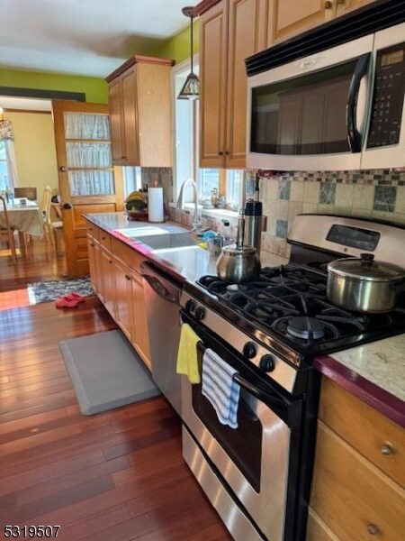 kitchen featuring decorative backsplash, sink, pendant lighting, appliances with stainless steel finishes, and dark hardwood / wood-style flooring