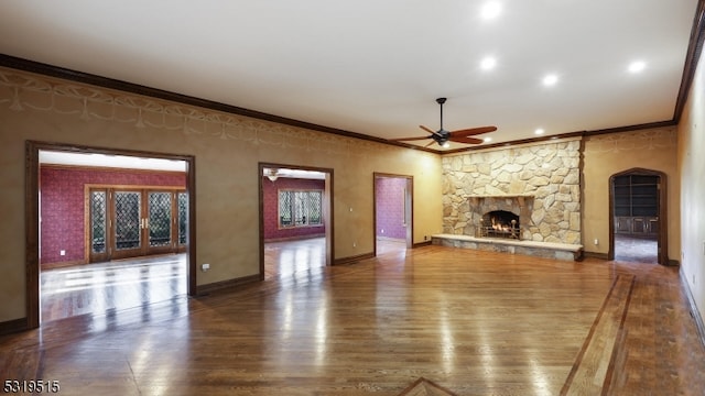 unfurnished living room featuring ceiling fan, hardwood / wood-style flooring, ornamental molding, and a stone fireplace