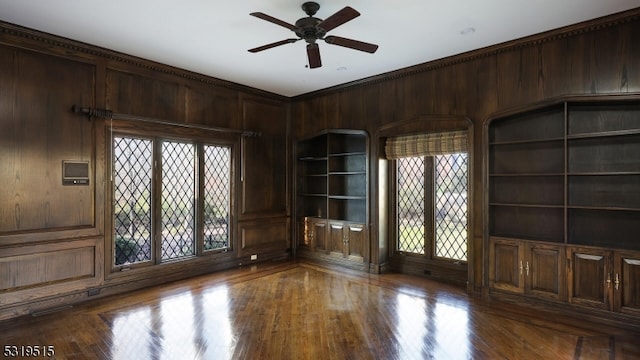 spare room with hardwood / wood-style floors, ceiling fan, wooden walls, crown molding, and built in shelves