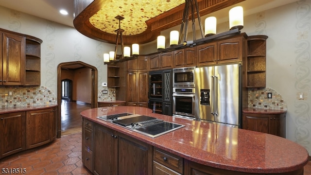 kitchen featuring backsplash, stainless steel appliances, decorative light fixtures, dark stone counters, and dark hardwood / wood-style floors