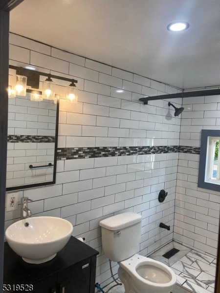 bathroom featuring tile walls, vanity, a tile shower, and toilet