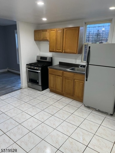 kitchen with sink, a baseboard heating unit, stainless steel gas stove, light hardwood / wood-style floors, and white refrigerator