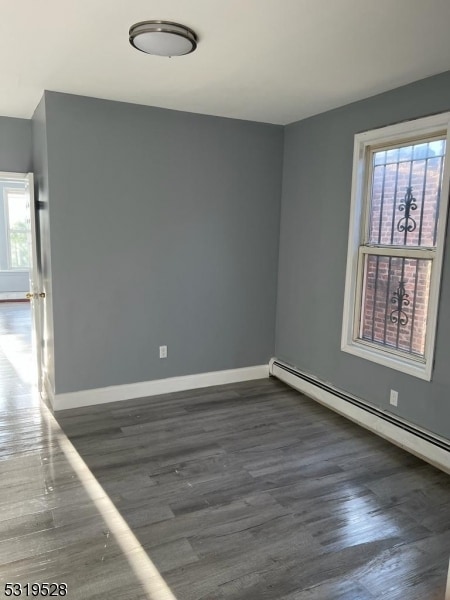 unfurnished room featuring dark hardwood / wood-style floors, a baseboard heating unit, and a wealth of natural light