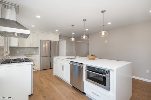 kitchen featuring stainless steel appliances, pendant lighting, white cabinets, range hood, and a center island with sink