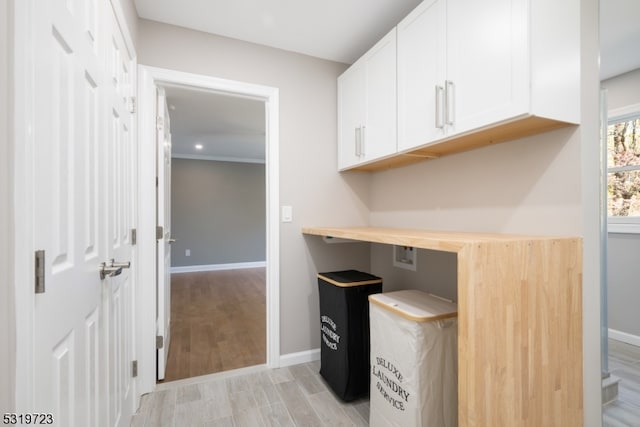 home office with crown molding, built in desk, and light wood-type flooring