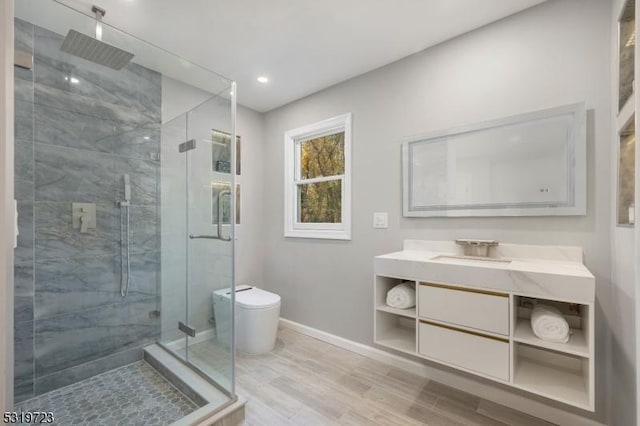 bathroom with vanity, toilet, a stall shower, baseboards, and wood finished floors